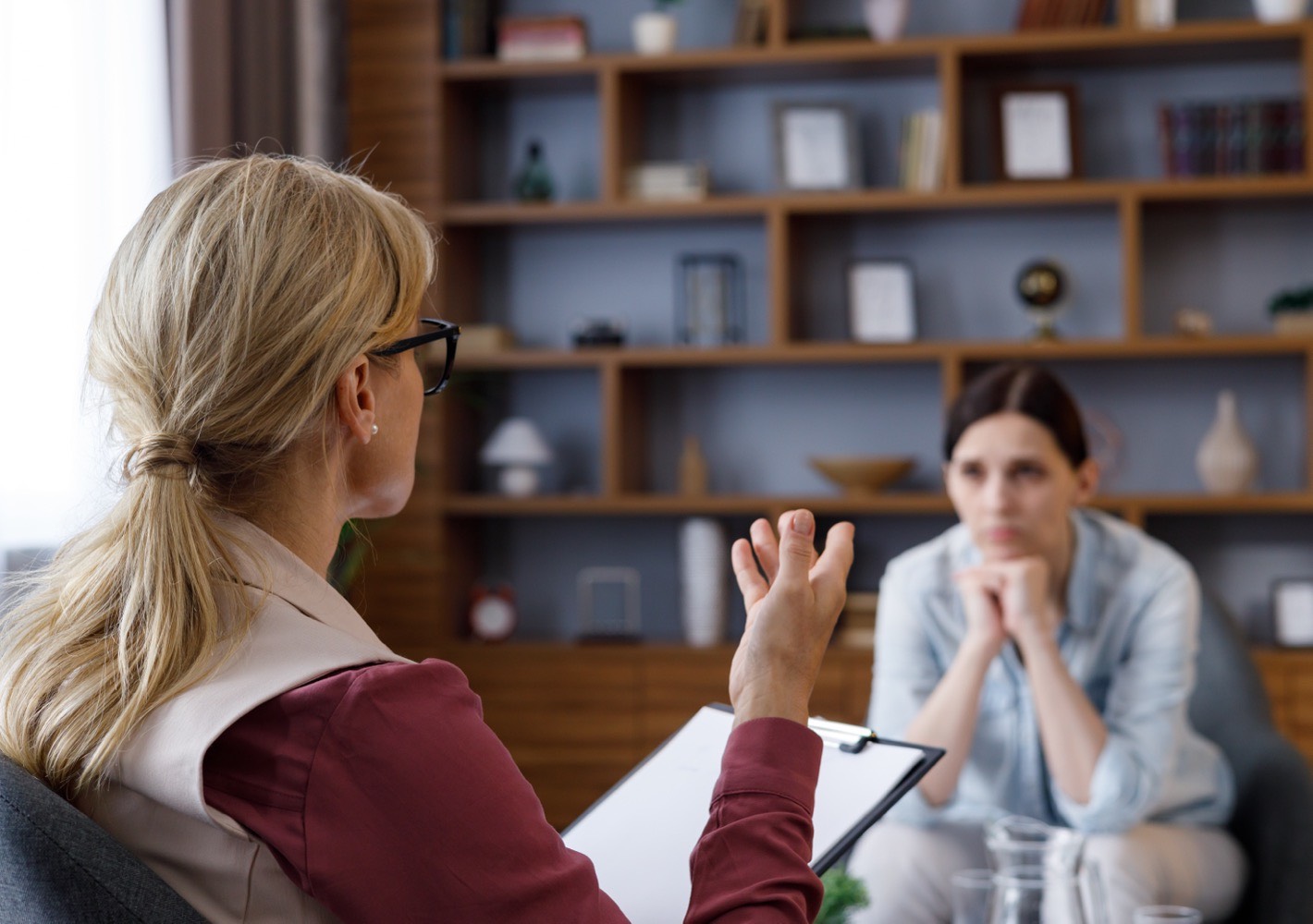 shoulder view female psychologist sitting armchair talking with upset woman patient psychologist taking notes clipboard psychology mental therapy mental health therapy session.jpeg